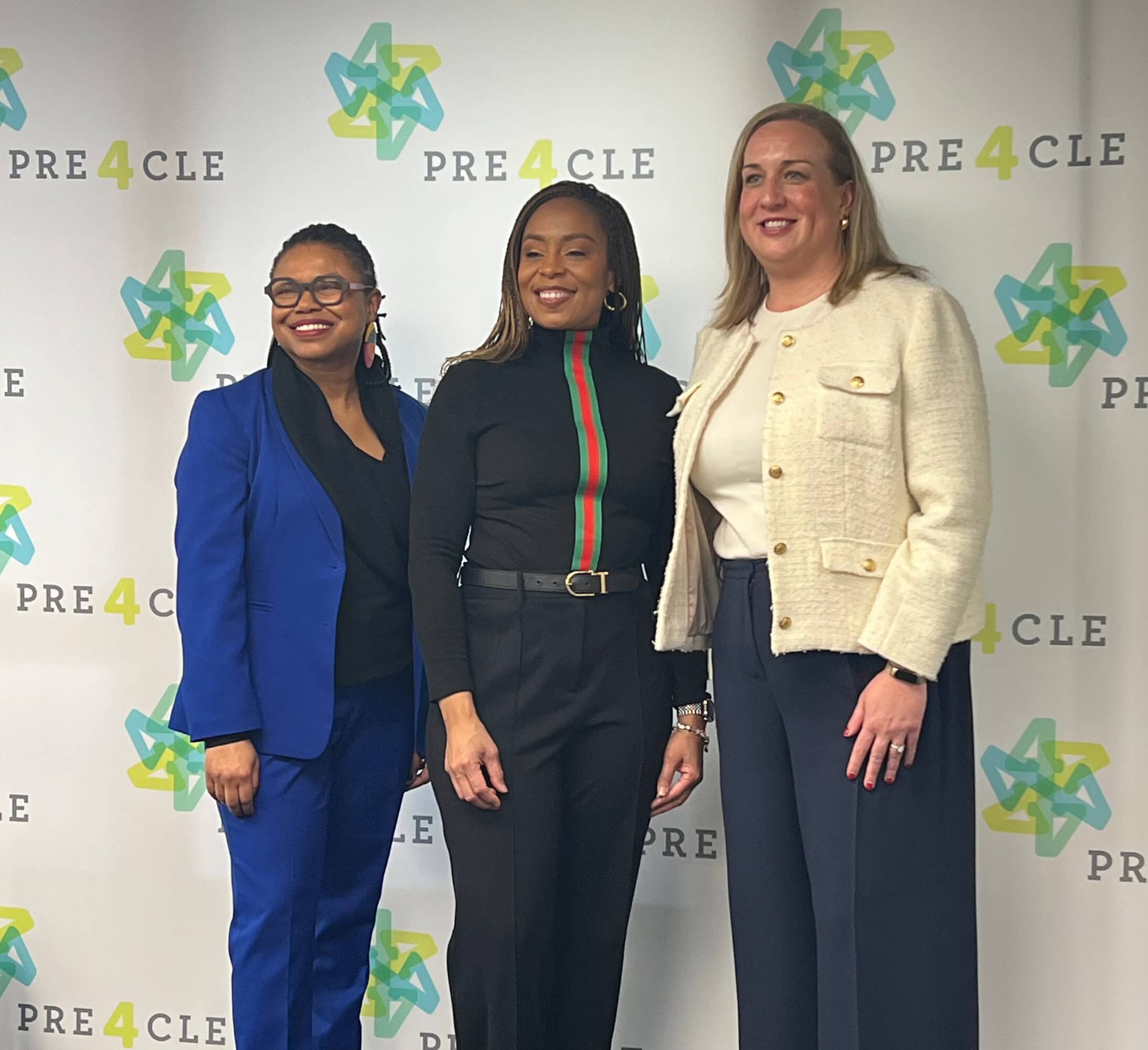 Three women stand in front of a PRE4CLE step-and-repeat banner, posing for a group photo.