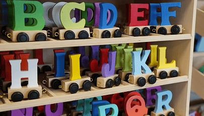 Wooden shelf holding colorful toy trains shaped like letters of the alphabet and vehicles such as tractors and a truck.