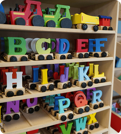Wooden shelf holding colorful toy trains shaped like letters of the alphabet and vehicles such as tractors and a truck.