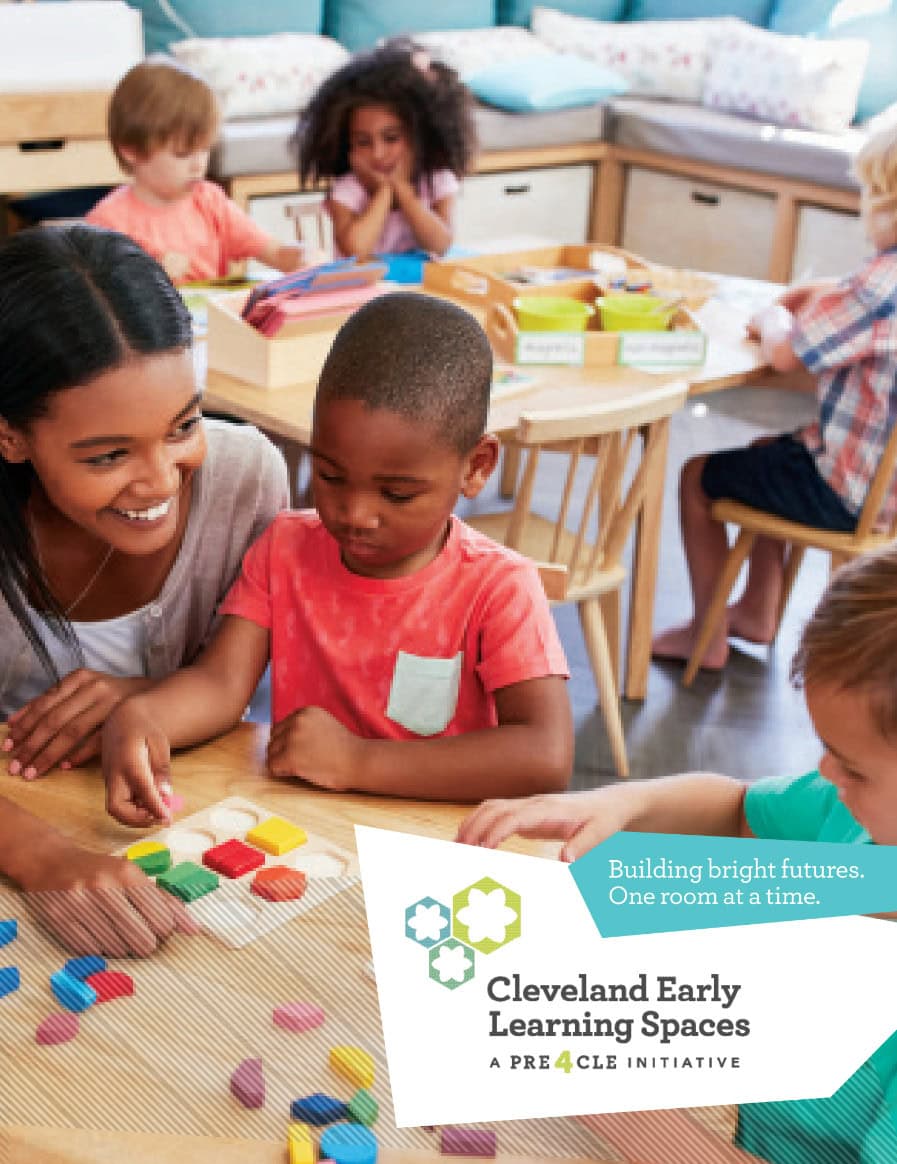 A teacher helps young children with a shape-sorting activity at a classroom table. Other children play and work together in the background. Cleveland Early Learning Spaces logo is in the corner.