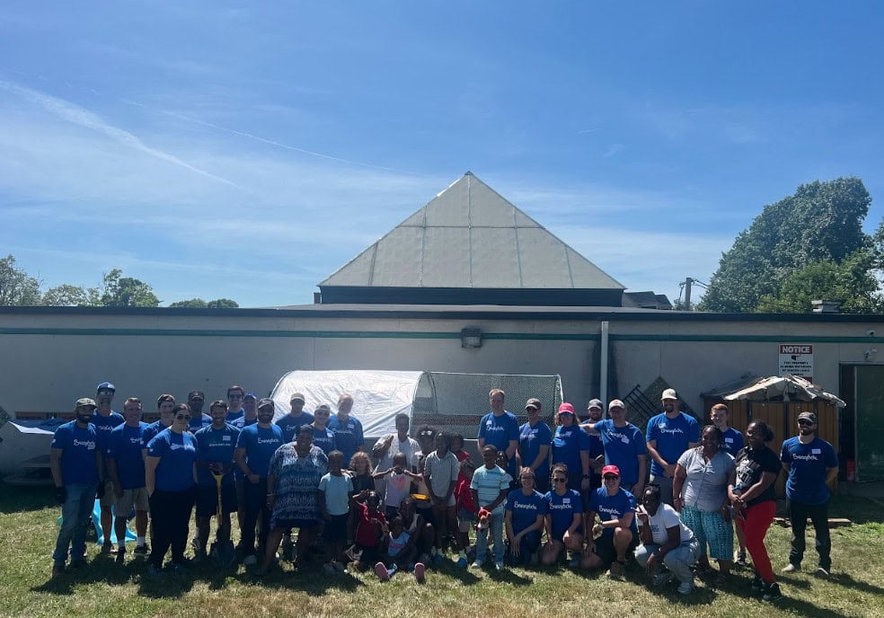 A group of people wearing blue shirts pose for a photo outdoors in front of a building on a sunny day.