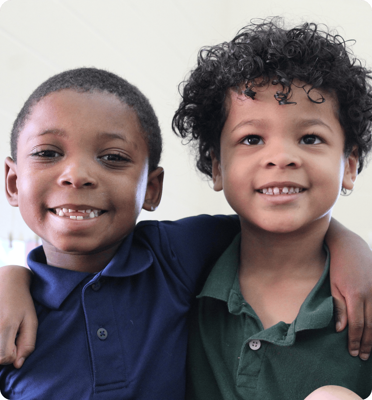 Two young children smiling, standing close together with arms around each other's shoulders, wearing collared shirts.